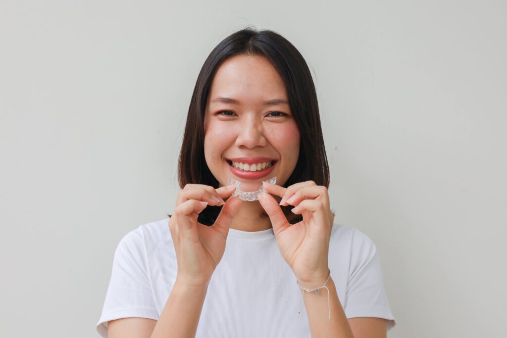 Woman smiling while holding Invisalign aligner