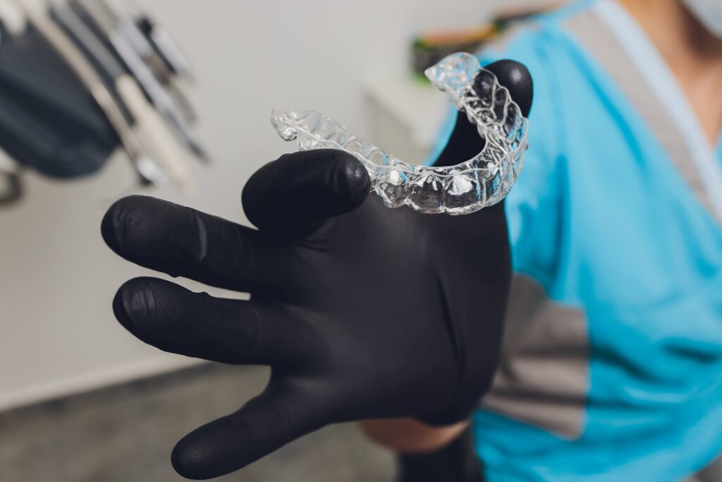 Orthodontist holding clear aligner with black glove